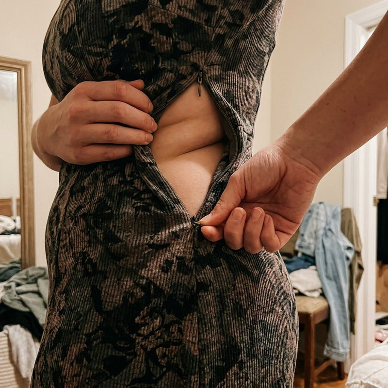 A woman unable to zip a fitted dress over her lower belly